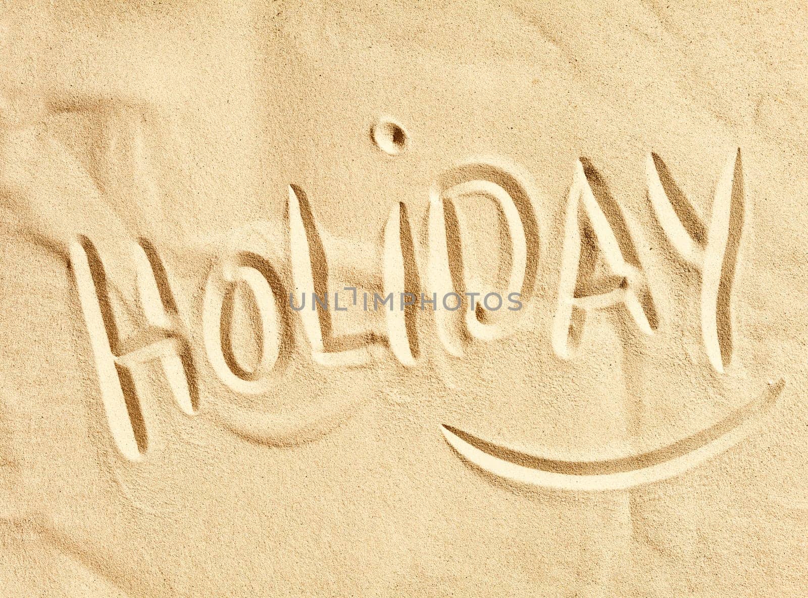 The word Holiday handwritten in golden beach sand in a conceptual image of summer vacations at the seaside, tourism and travel