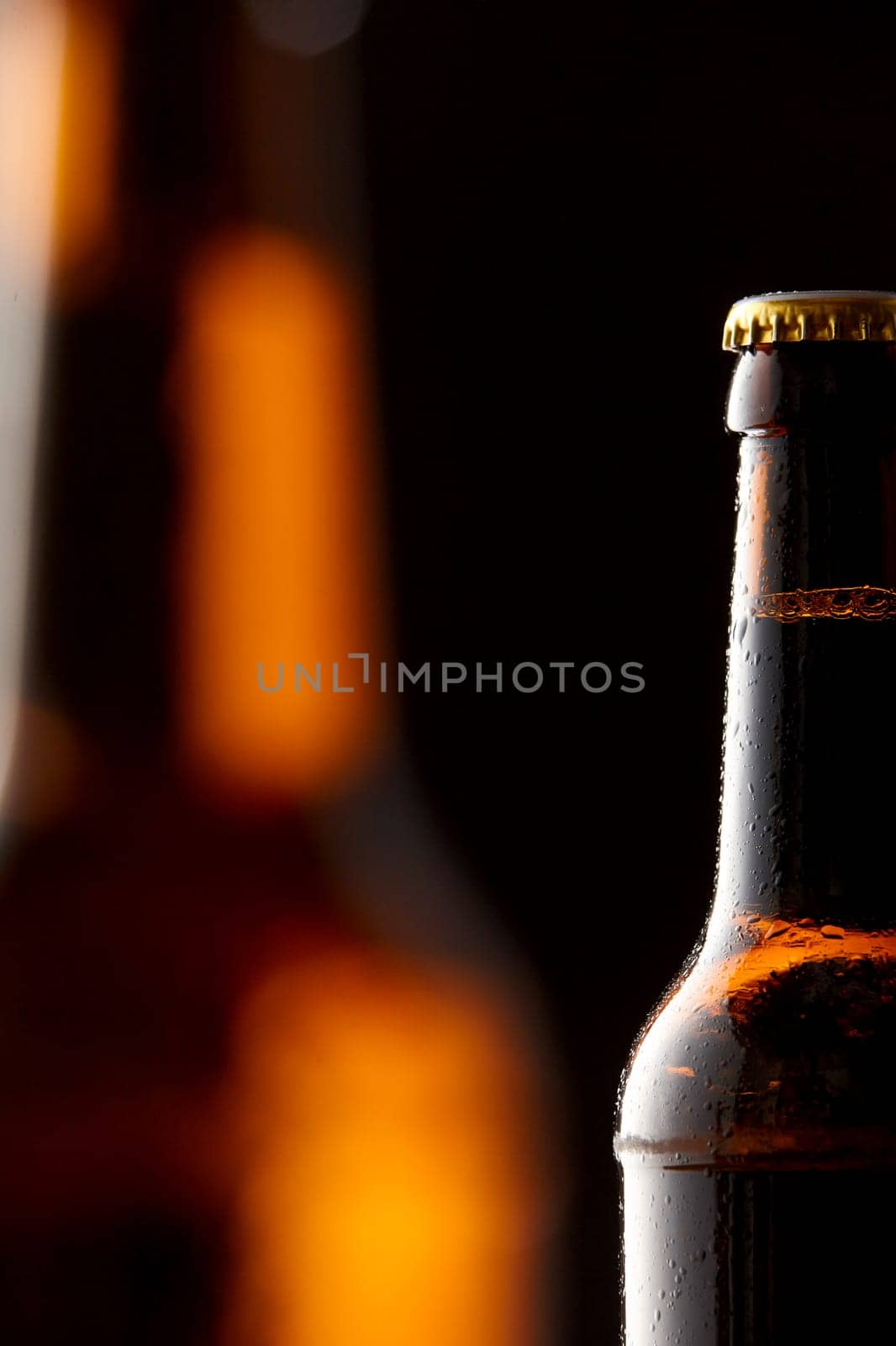 Partial view of a refreshing ice cold beer in a bottle for an Oktoberfest concept with copy space over a second blurred glowing beer on a dark background