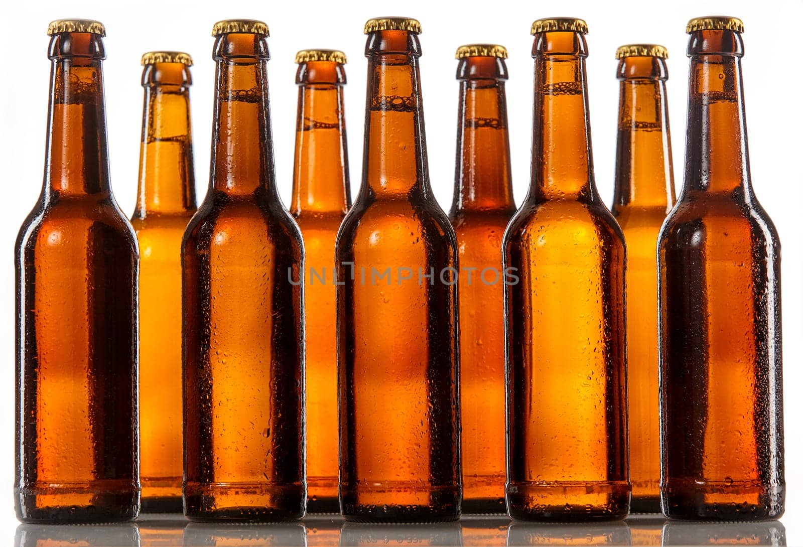 Unlabeled beer bottles standing two rows deep with metal caps and covered in condensation against a white background
