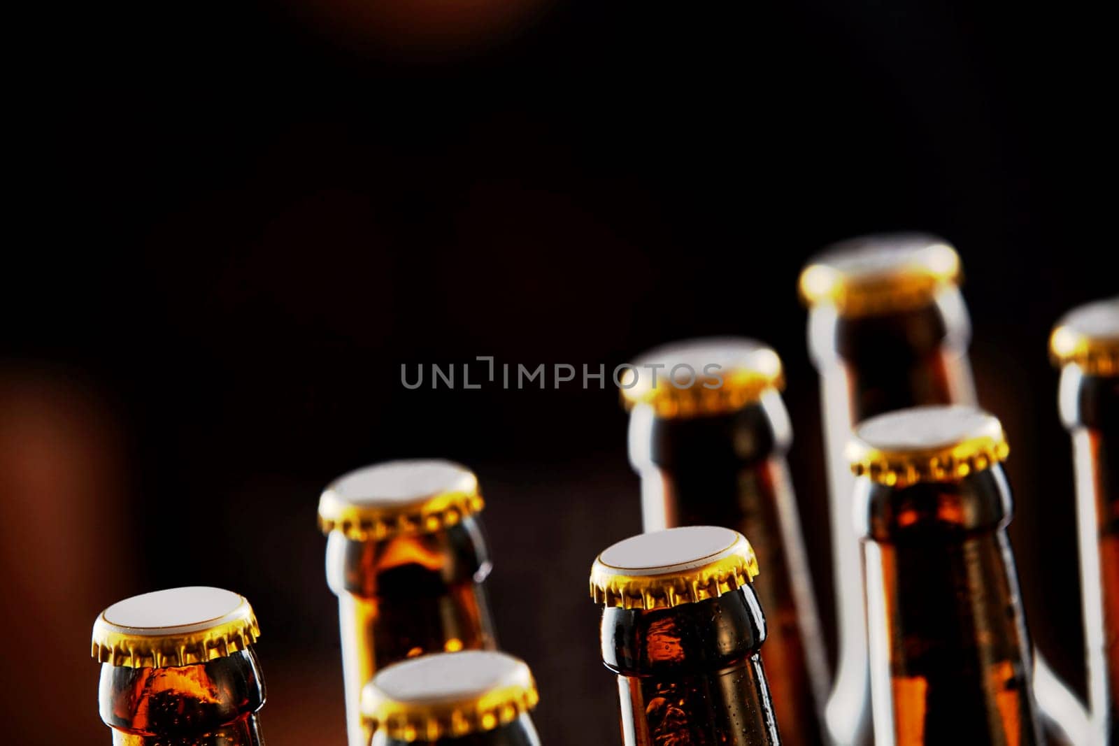 Two rows of unopened brown beer bottles in a closeup diagonal view over a dark background with copy space