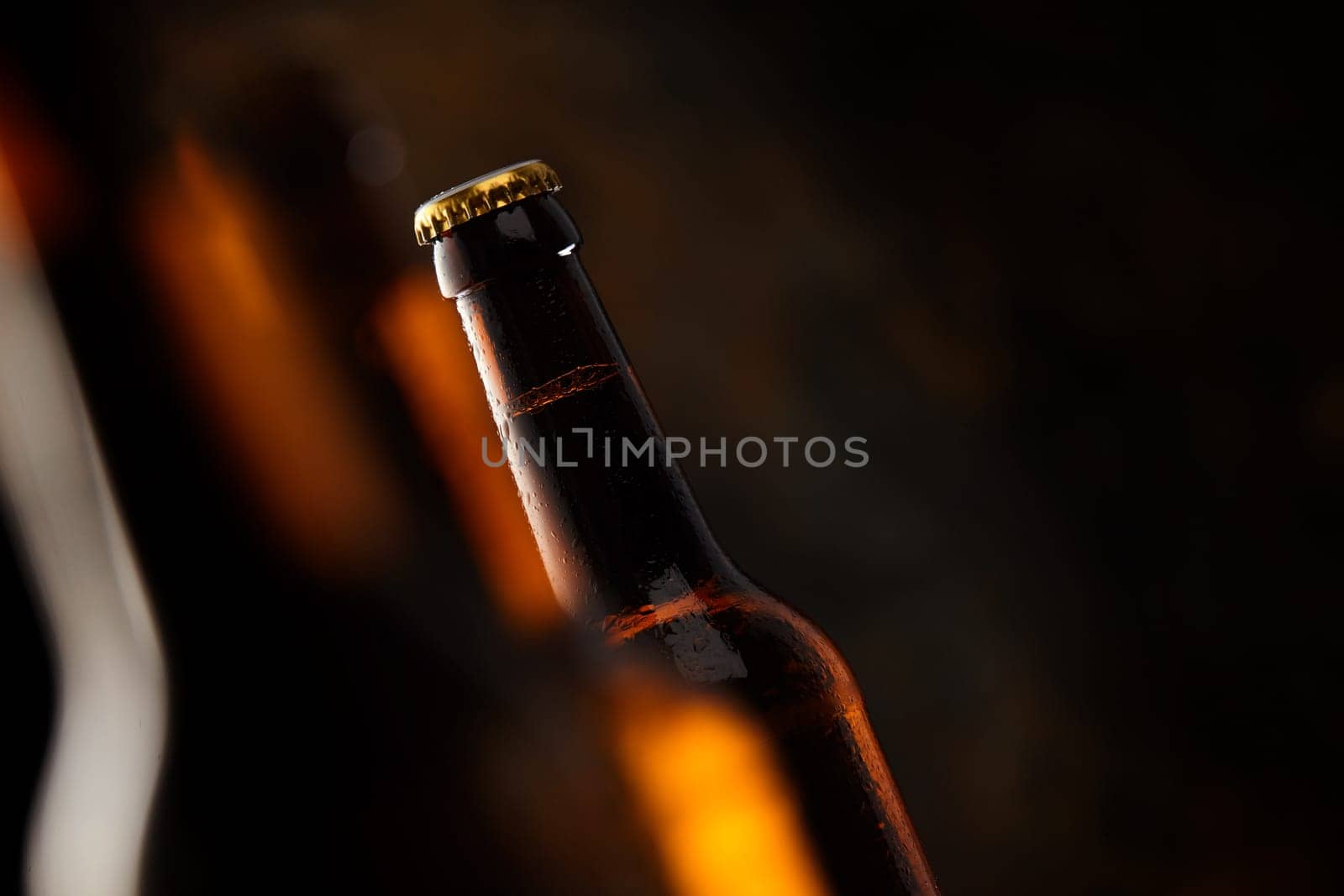 Tilted angle view of an unopened unlabelled glowing beer bottle with selective focus and shadowy dark copy space conceptual of a tavern and Oktoberfest