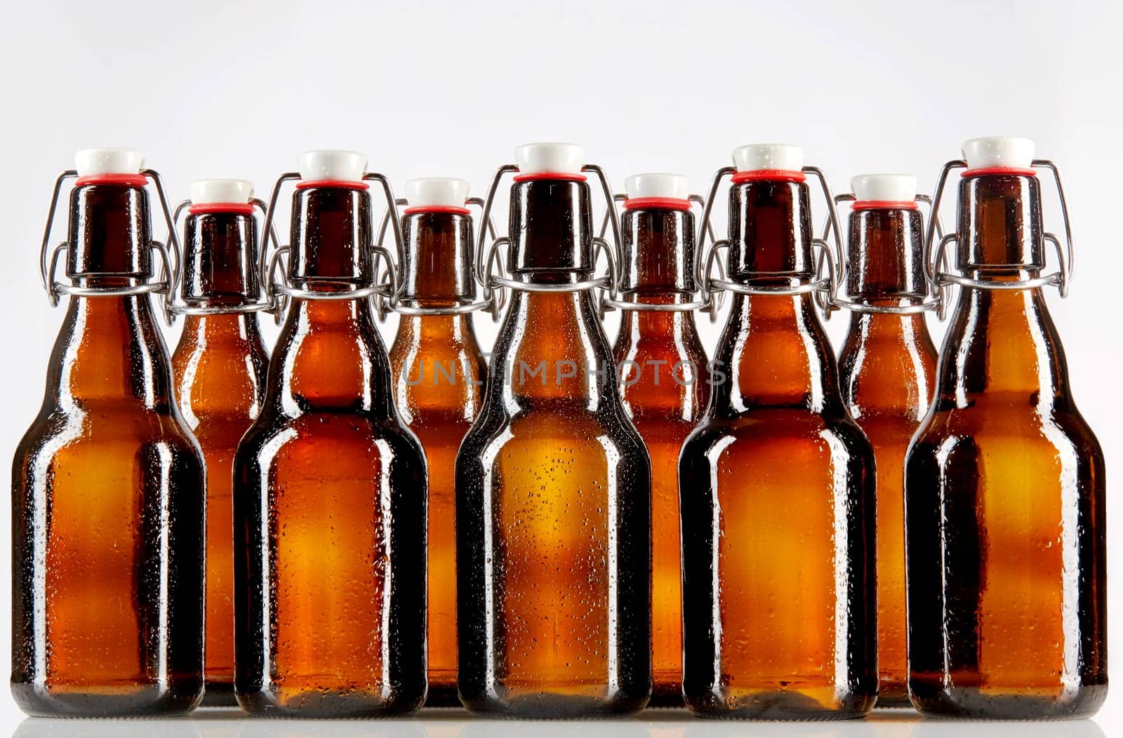 Two rows of nine tall blank glass bottles with copy space used for beer or other commercial beverages over gray background