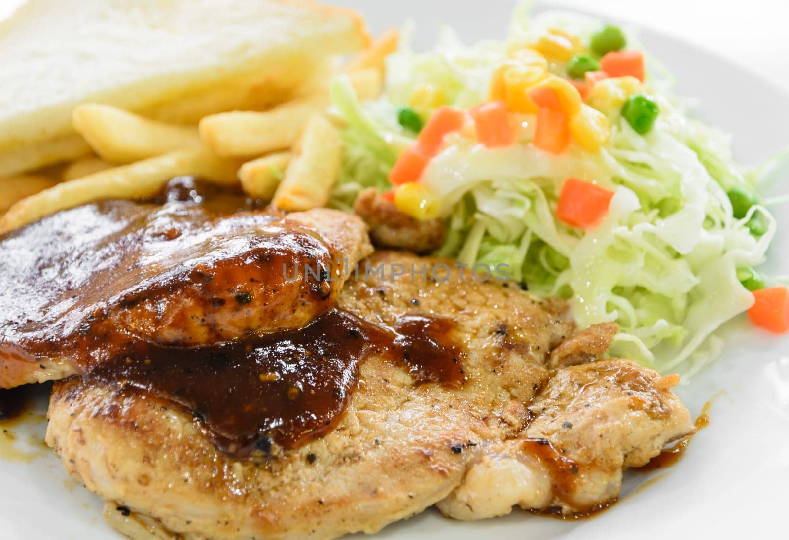 Grilled pork steak fillet with black pepper sauce, vegetable salad, bread and french fries on white plate