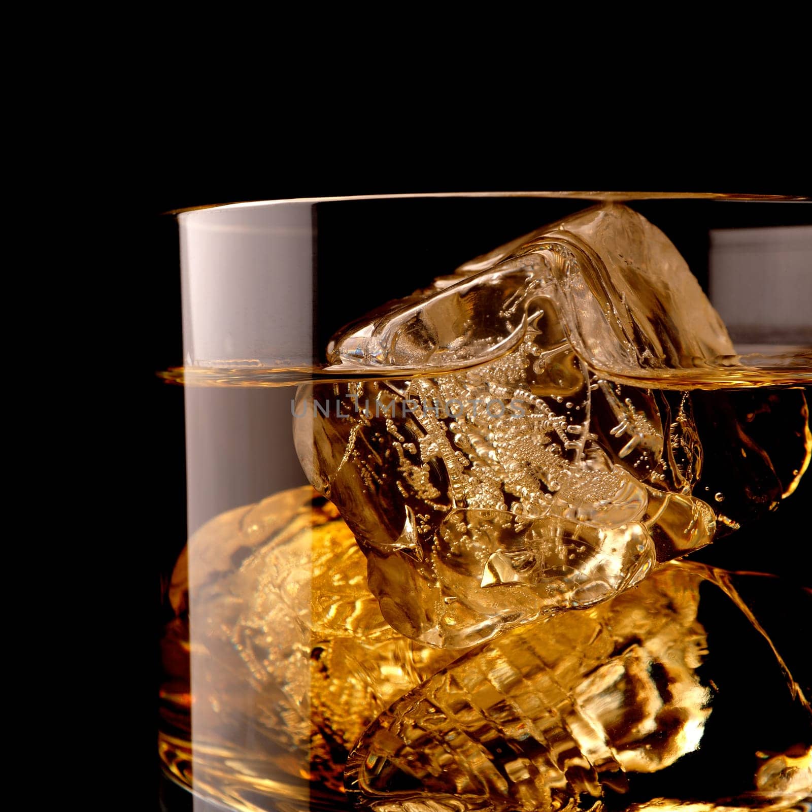 Close up shot of a glass of whiskey with ice cubes on a black background