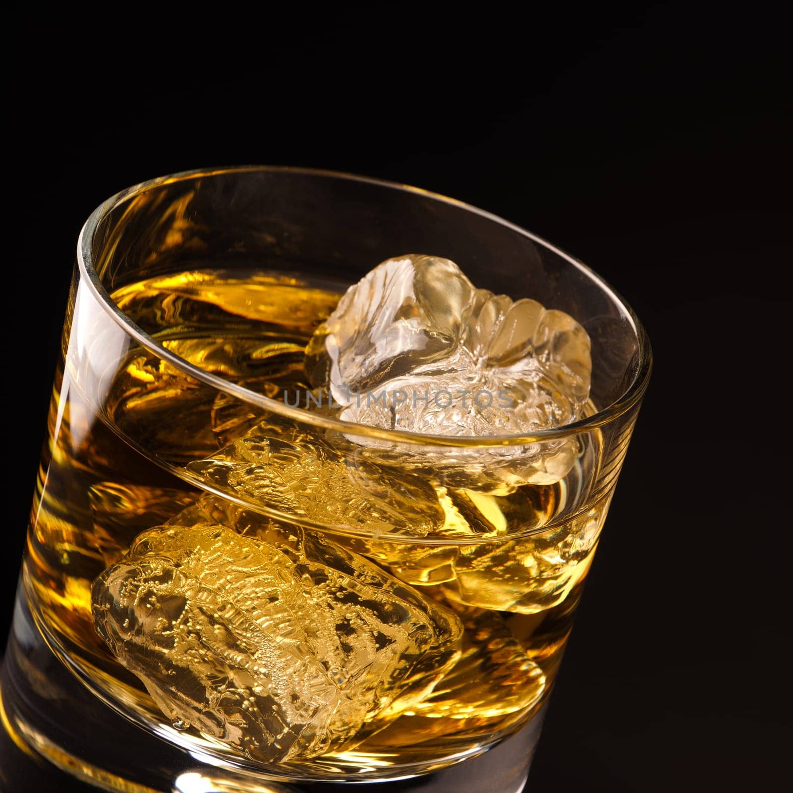Close up shot of a glass of whiskey with ice cubes on a dark background
