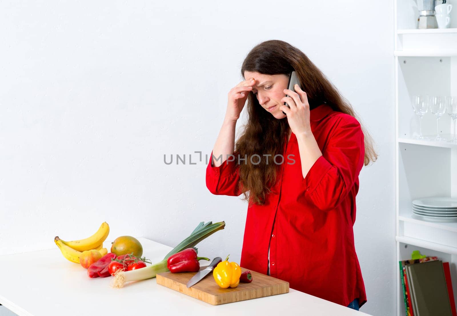 dark haired woman with red shirt in the kitchen is calling
