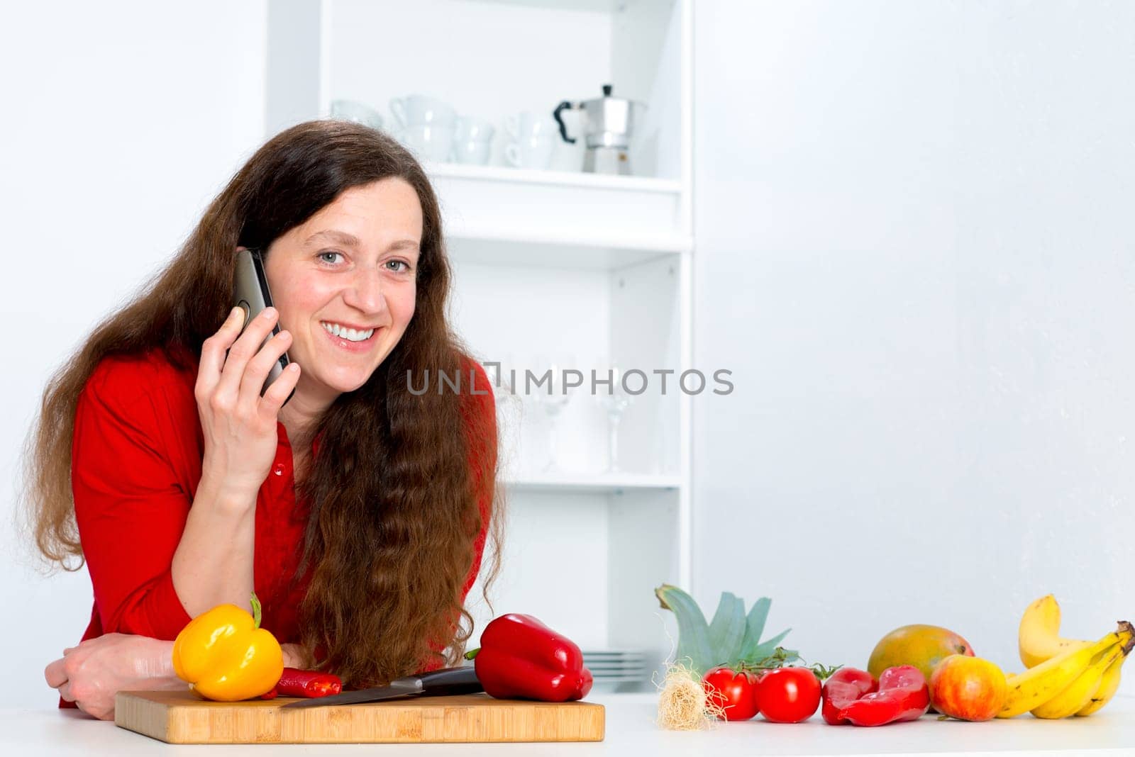dark haired woman with red shirt in the kitchen is calling