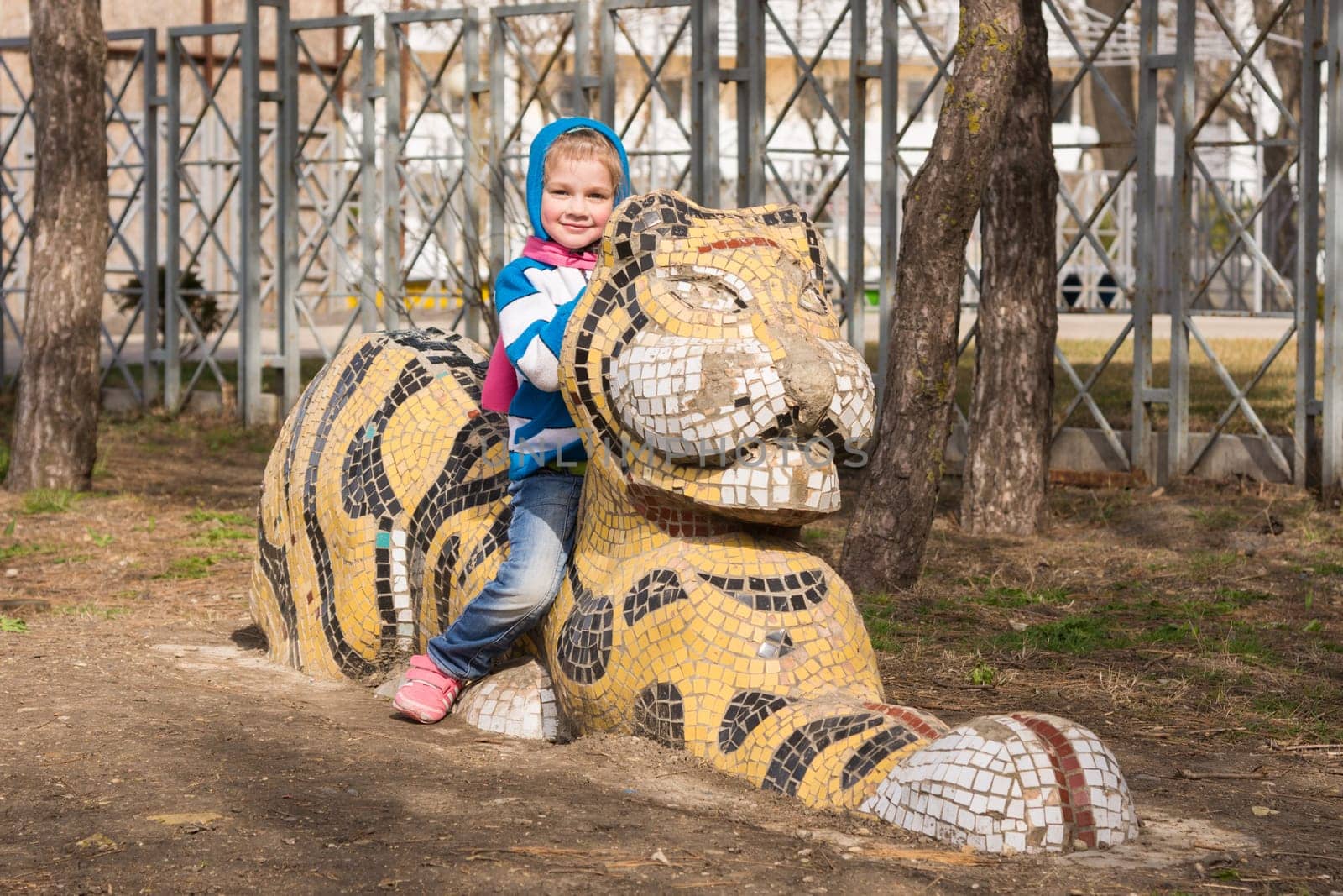 Happy girl sitting on a sculpture of a tiger on the playground in Anapa