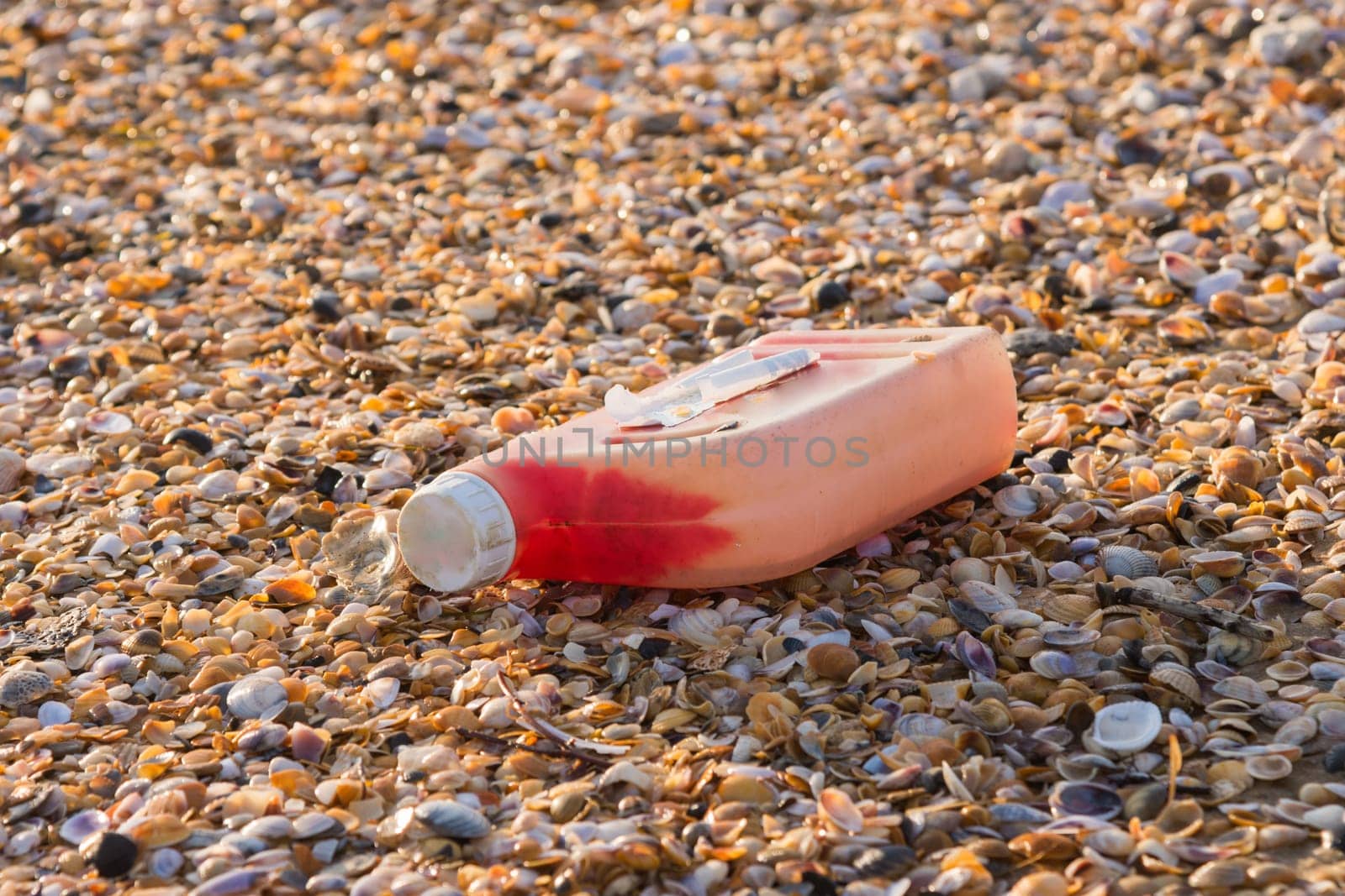 Plastic bottles of engine oil on the beach is strewn with small colorful sea shells