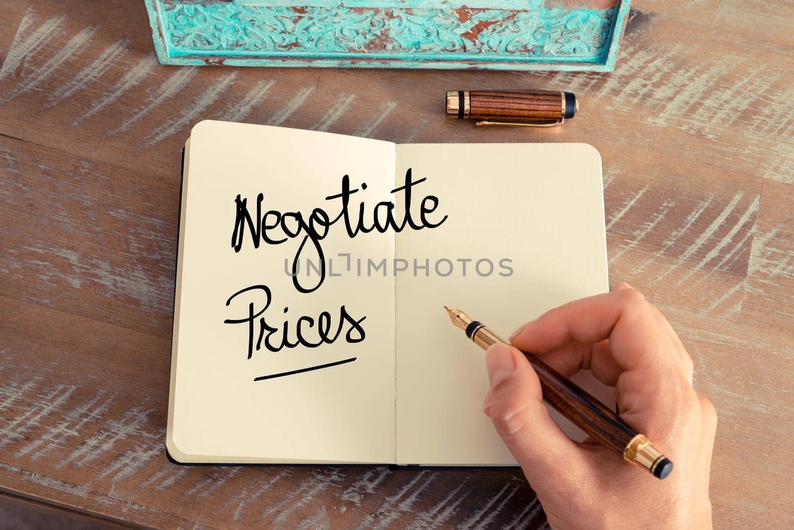 Handwritten text Negotiate Prices as concept image. Retro effect and toned image of a woman hand writing a note with fountain pen on a notebook.