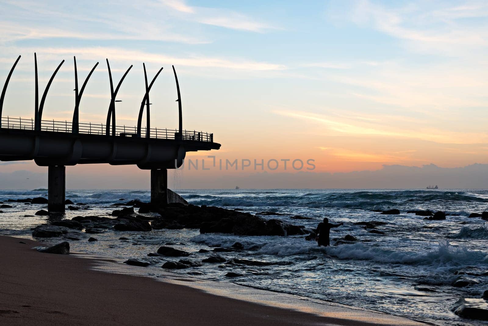 Man performing religious ritual next to the Millennium Pier in Umhlanga Rocks at Sunrise, with ships on the Indian Ocean in the background