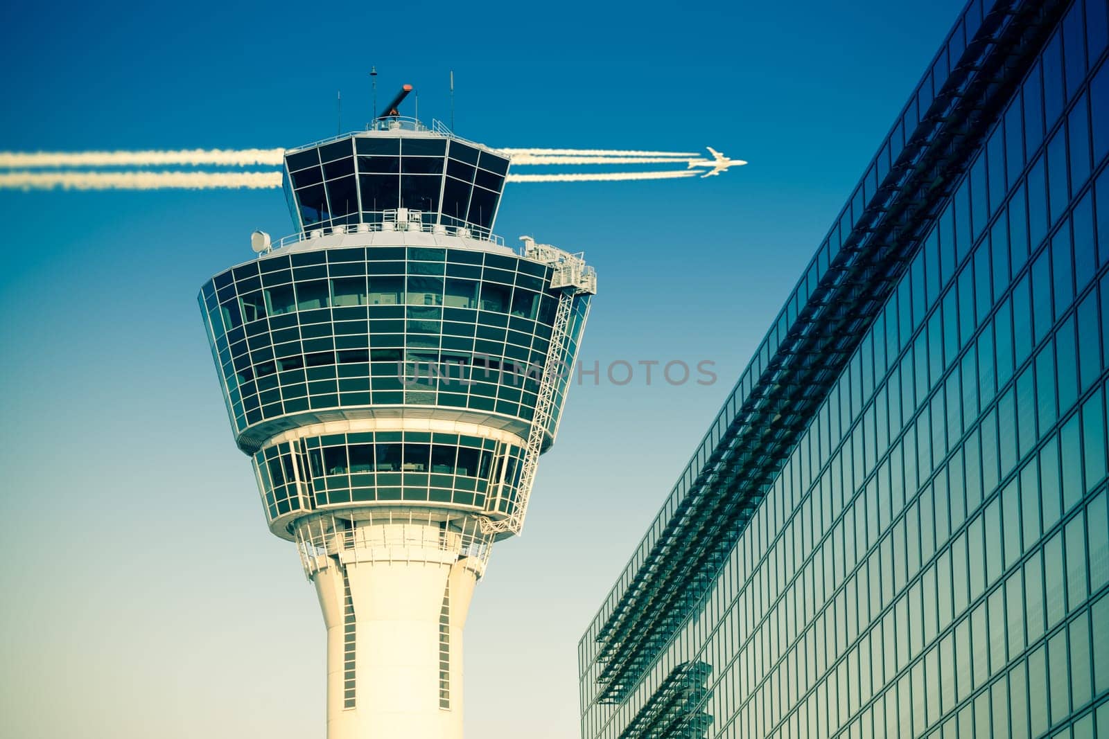 Flights management air control tower and passenger terminal in Munich international airport with flying plane in clear sky. Stock photo with split toning effect.