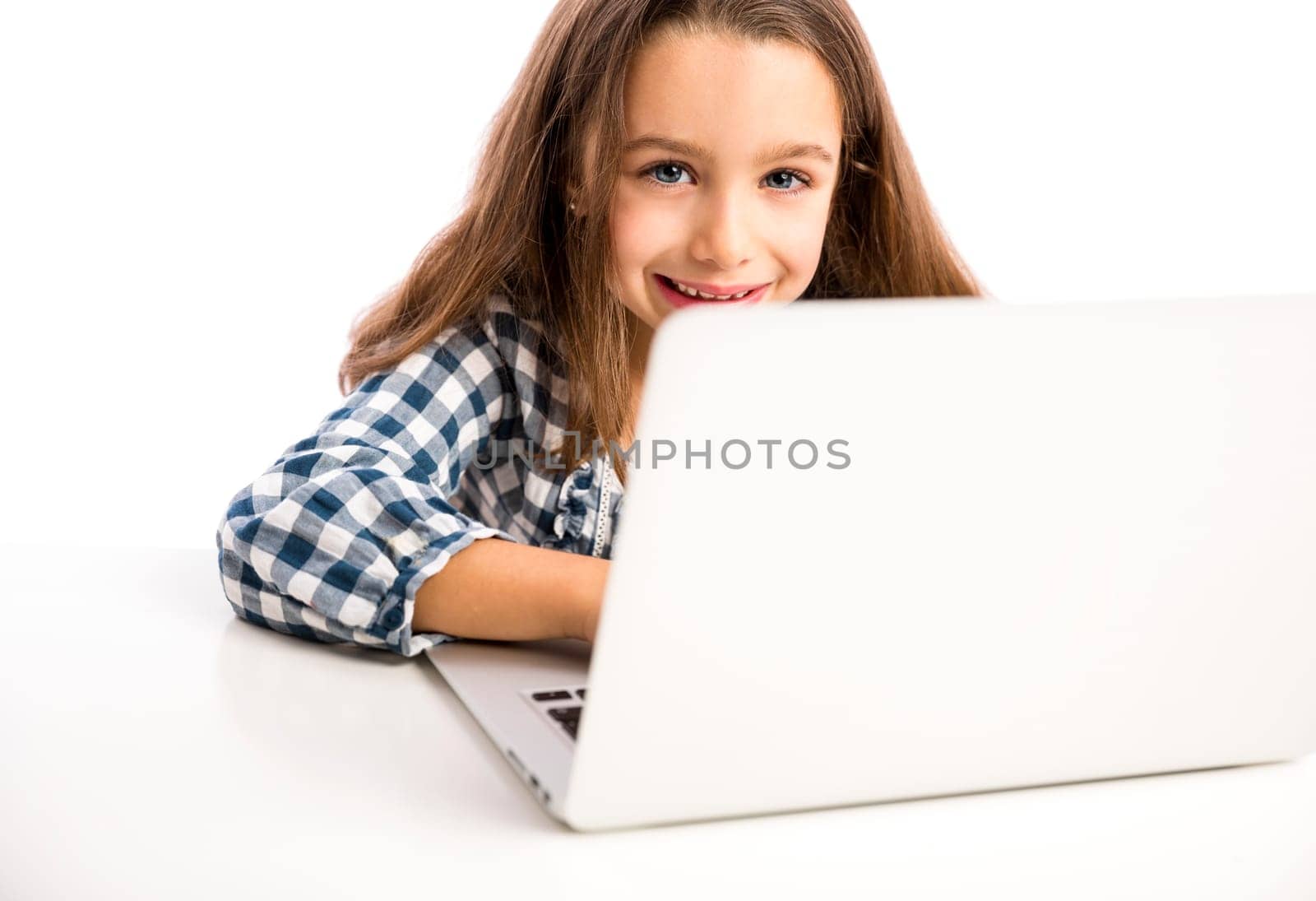 Happy little girl sitting on a desk and working with a laptop