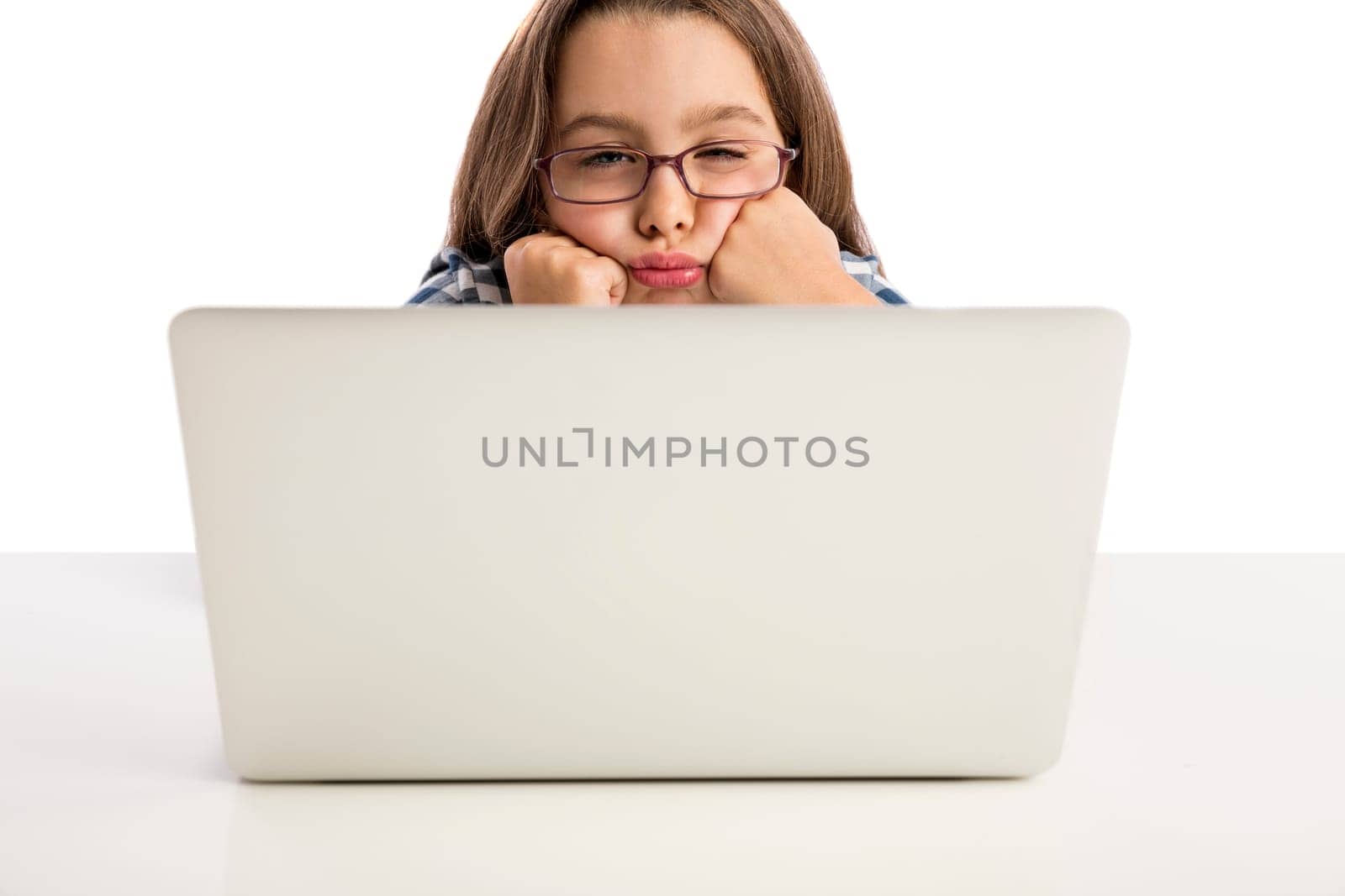 Happy little girl sitting on a desk and working with a laptop