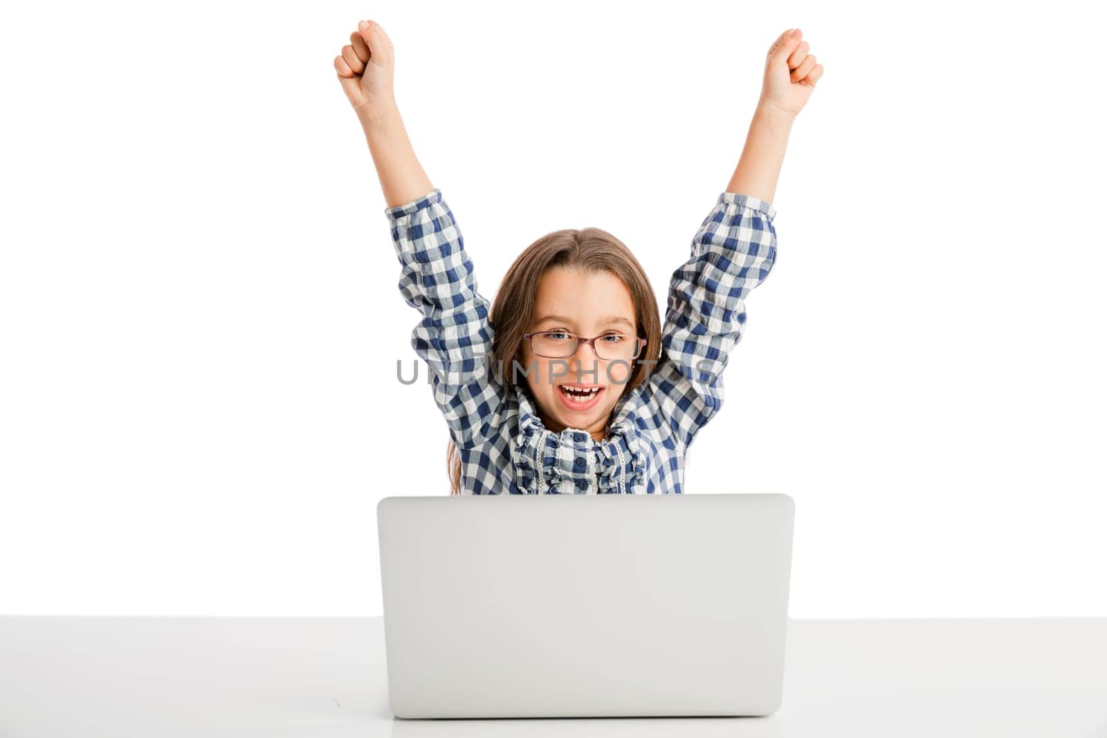 Happy little girl sitting on a desk and working with a laptop