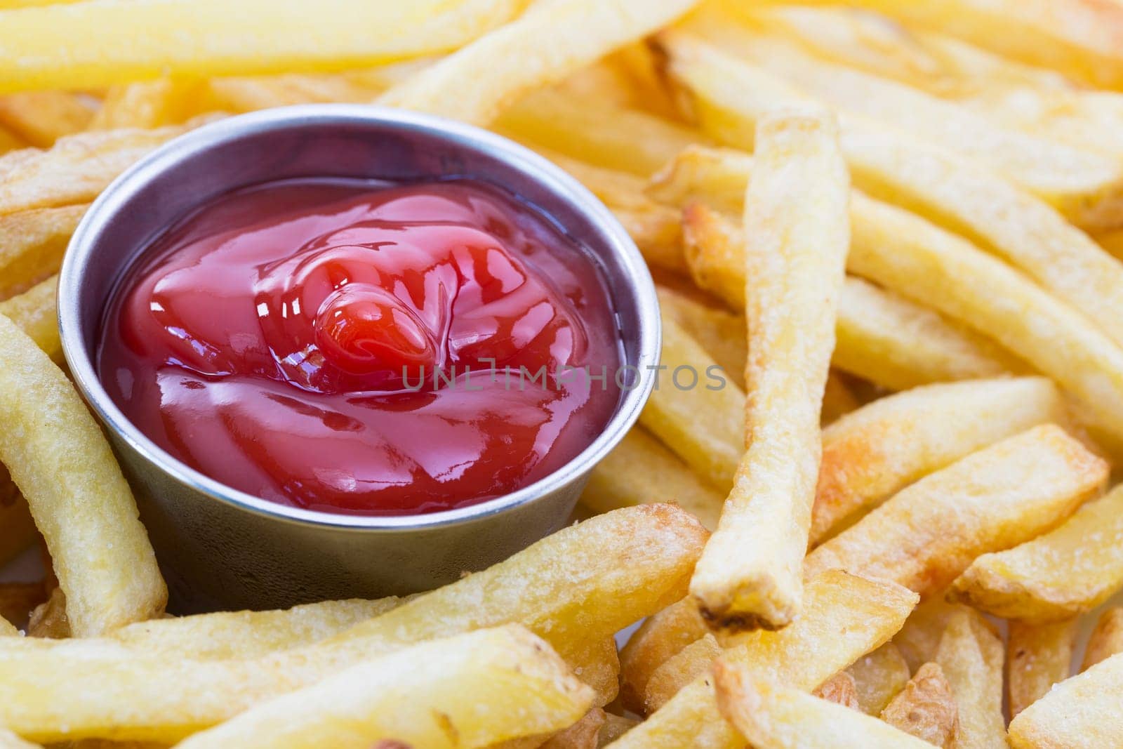Close up shot of french fries surrounding cup of ketchup.
