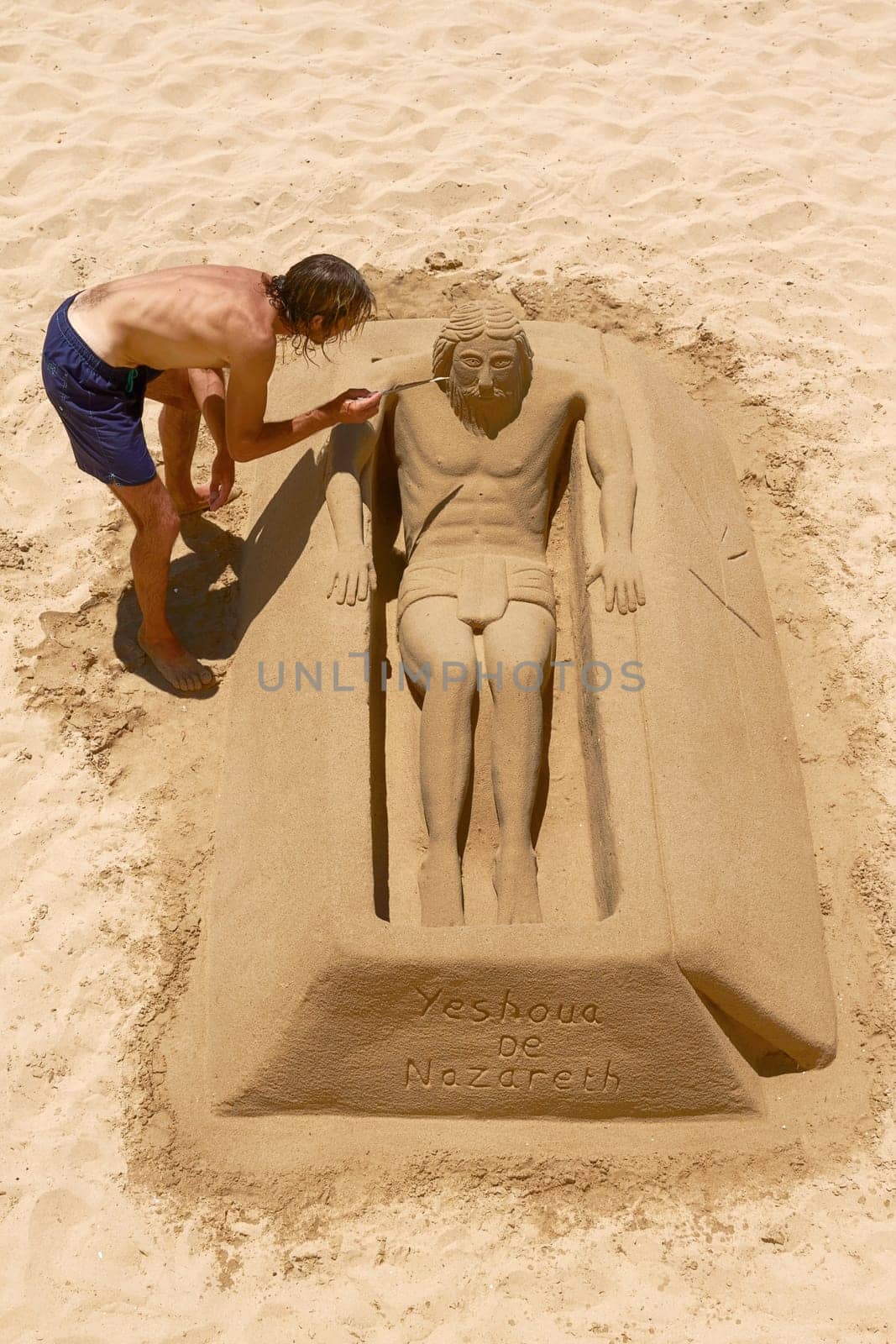 Young Man Working on Sand Sculpture of Jesus in Cadiz, Spain.