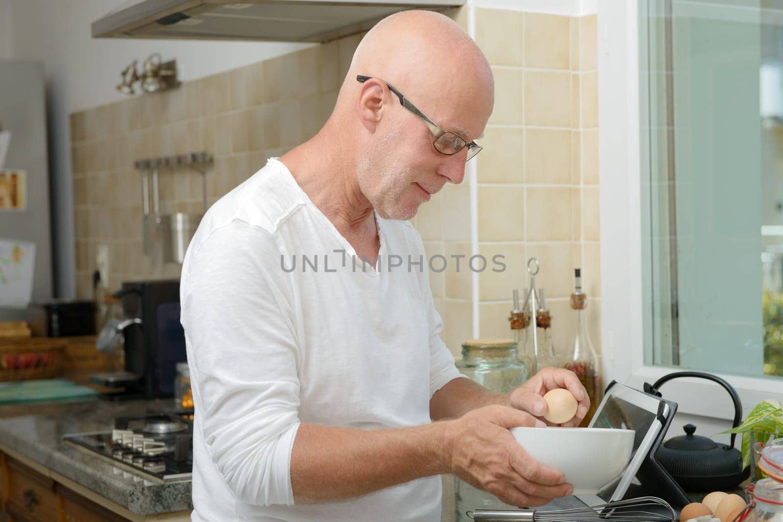 a mature man breaks an egg in the kitchen