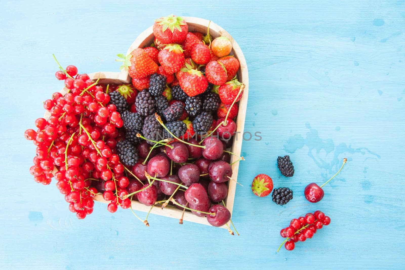 Fresh red fruits in heart shape on a rustic blue background