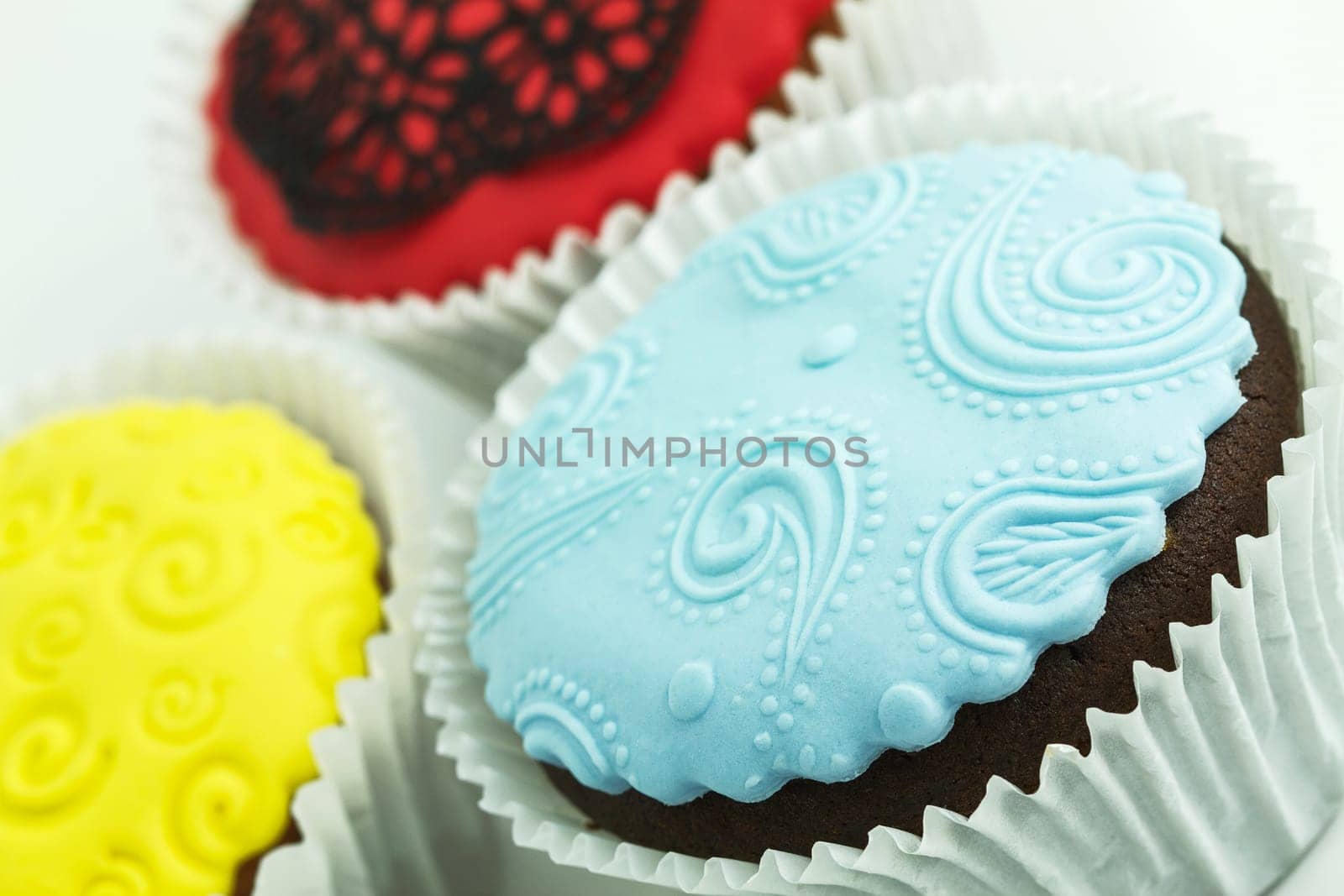 Three cupcakes on the white background. Yellow, blue and red with handmade decoration