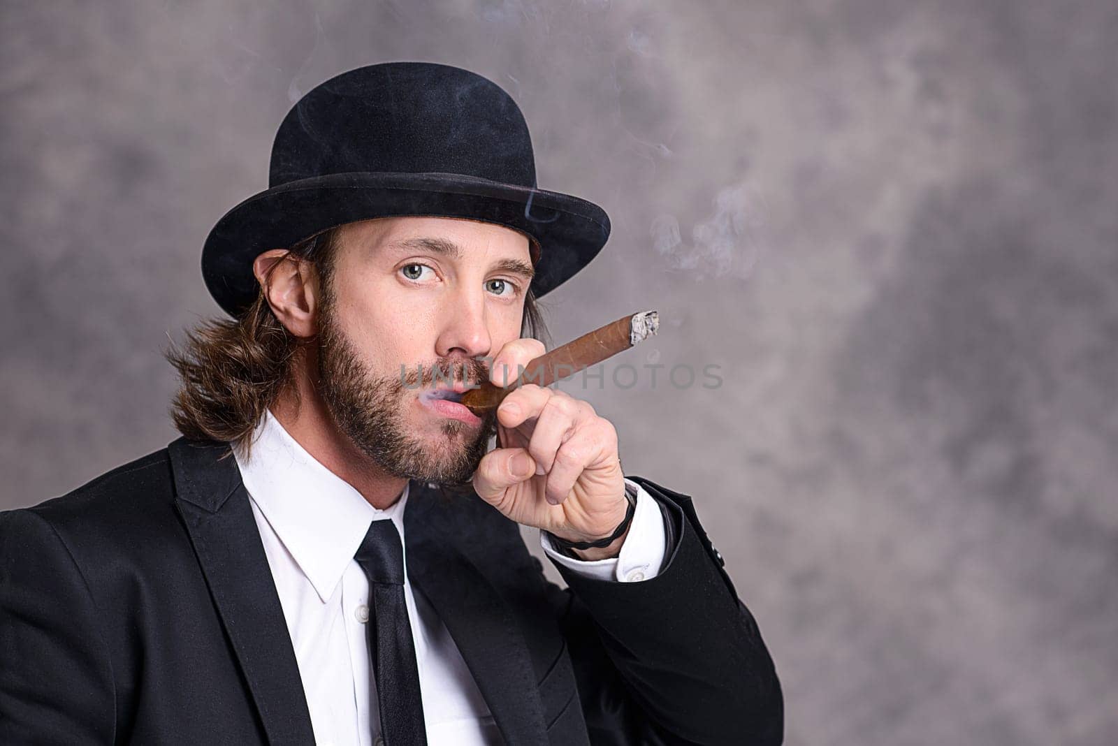 young businessman with bowler hat in black suit smoking big cigar