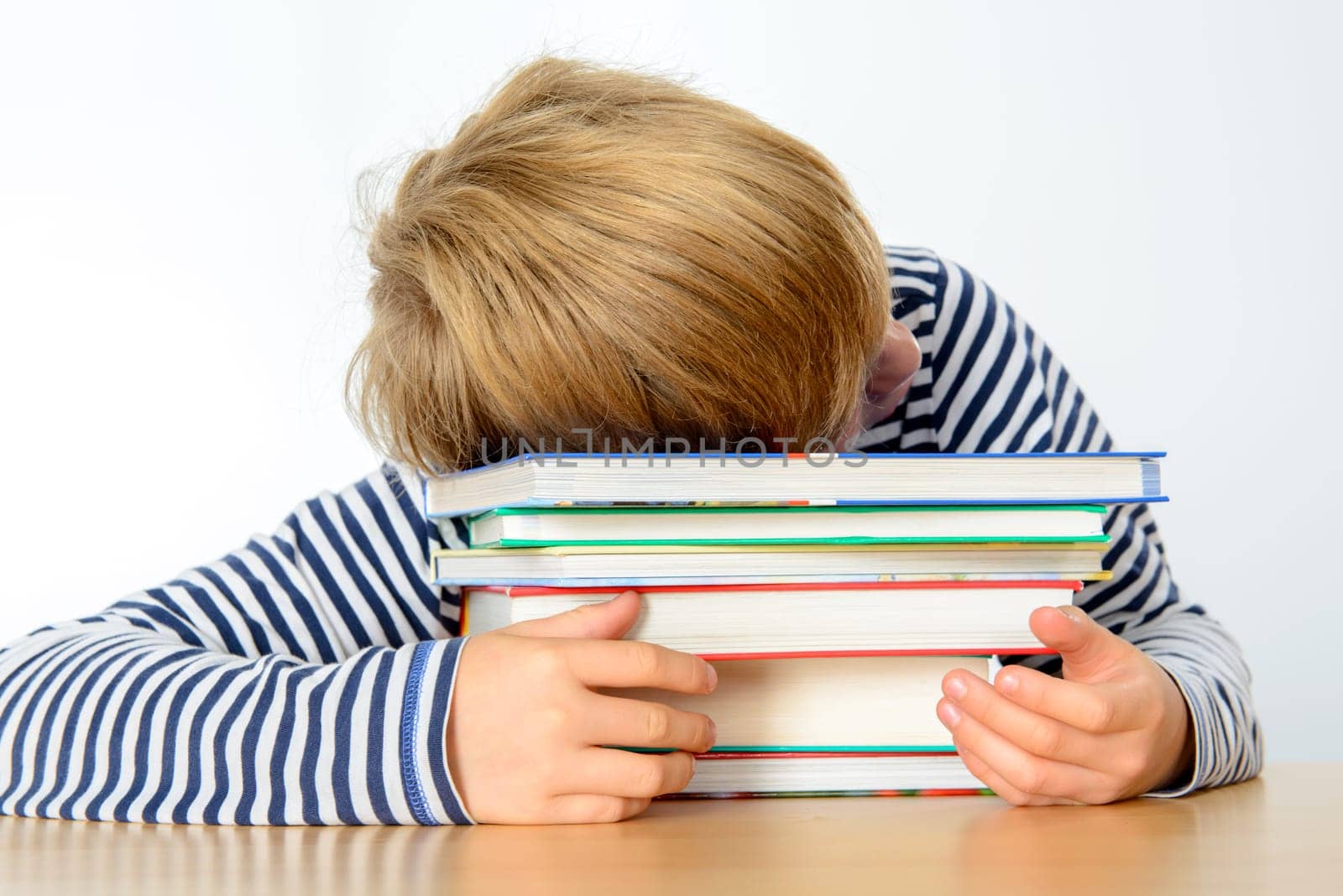 tired blond boy on a pile of books