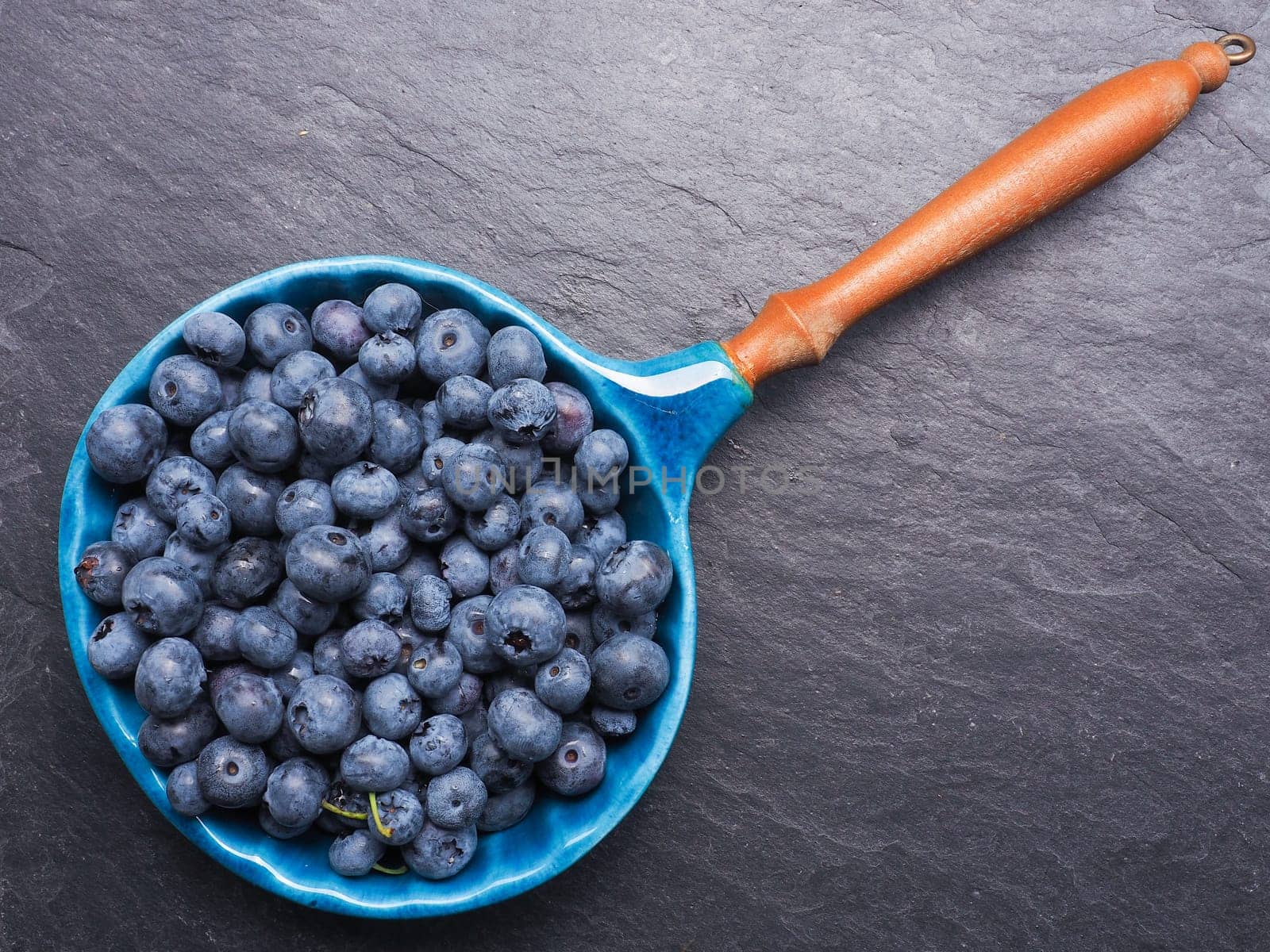 Fresh blueberries in a rustic bowl on dark slate