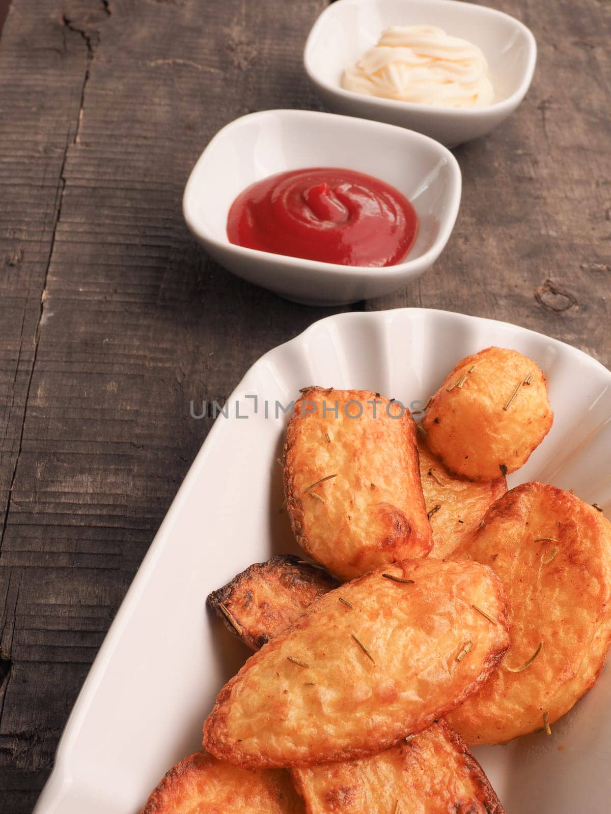 Rosemary potatoes with ketchup and mayonnaise on an old wooden kitchen table