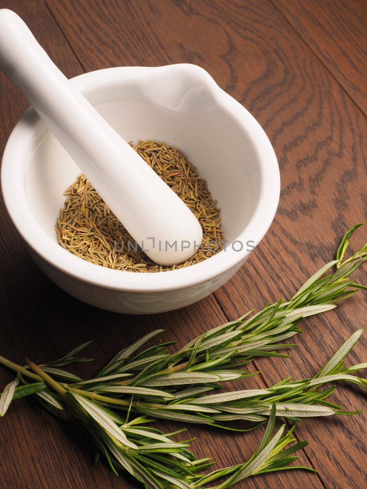 White porcelain mortar and pestle with rosemary on a wooden table