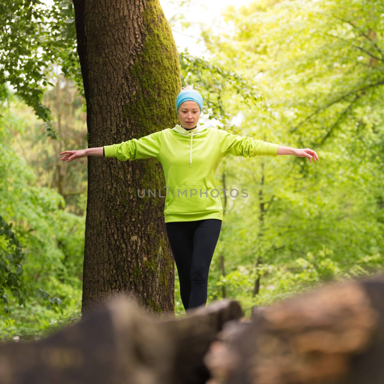 Active sporty woman holding balance on tree trunk while workout in nature. Wellness and healthy lifestyle concept.