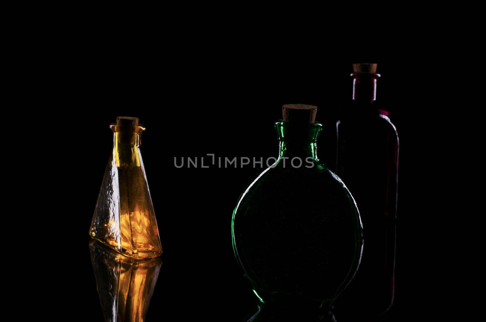 three colored decorative bottles on glass plate against a black background