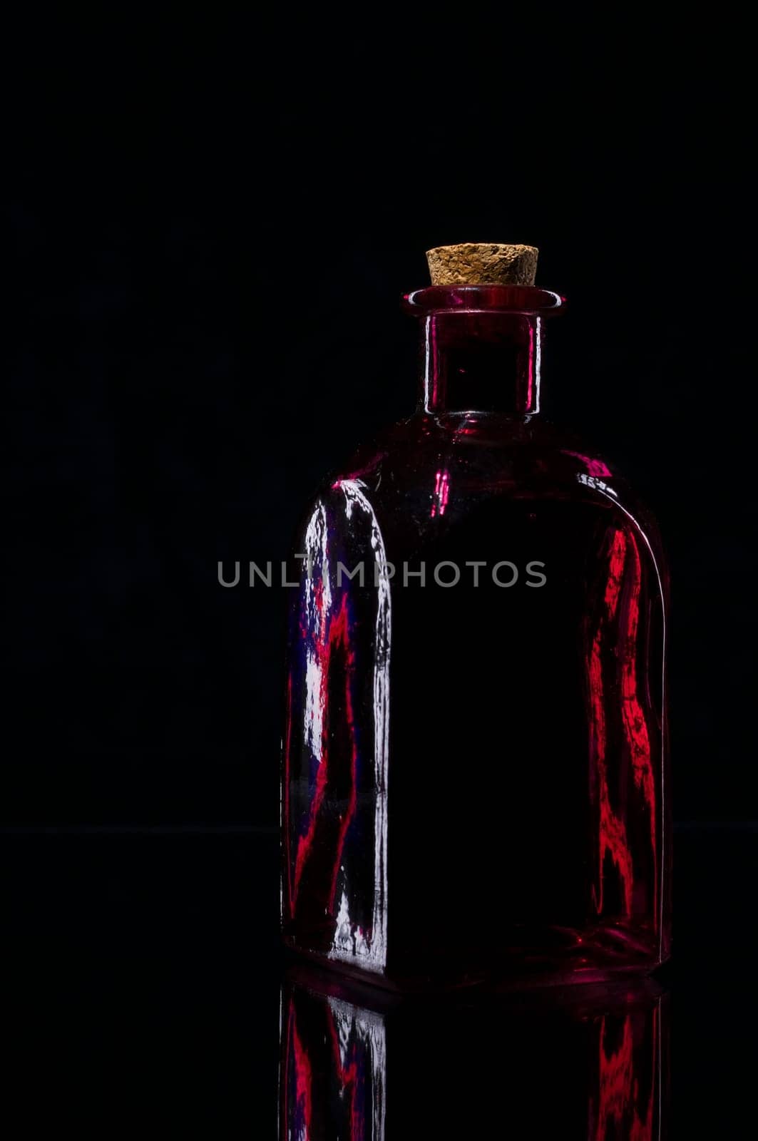 Still life of a red angular bottle with border light against a black background