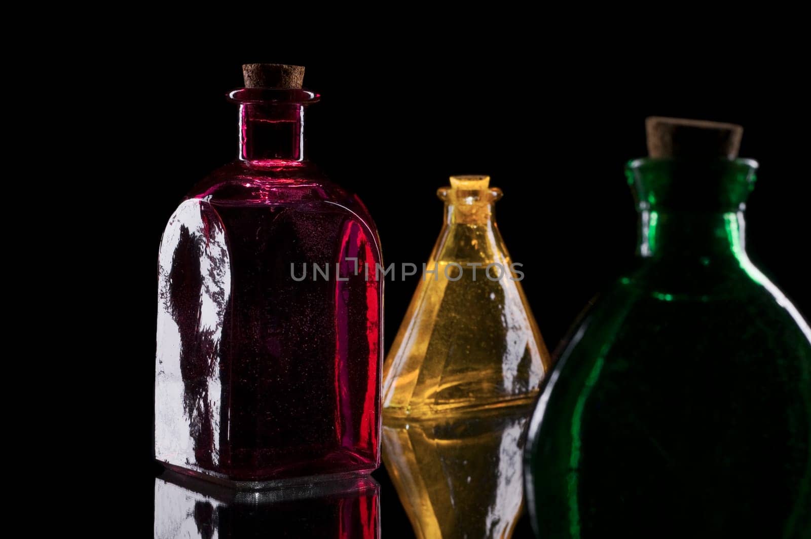 three colored decorative bottles on glass plate against a black background