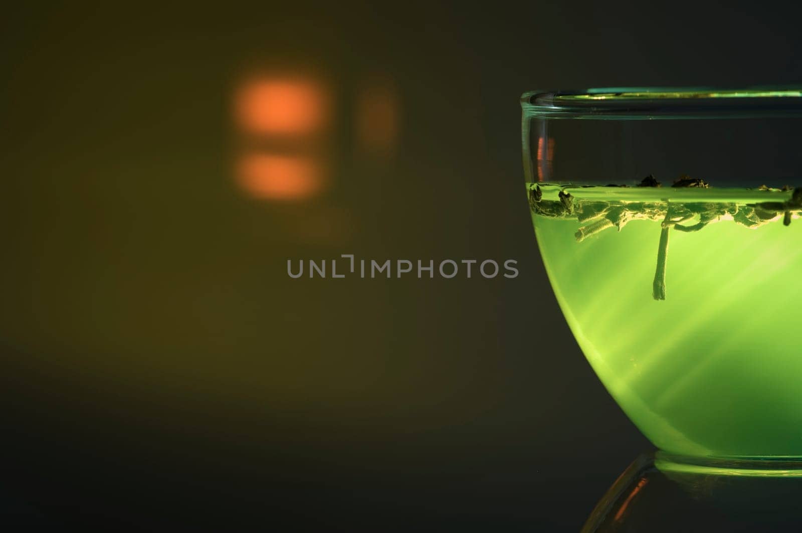 Cut close-up of a glass cup against a green illuminated background with a bright reflection.