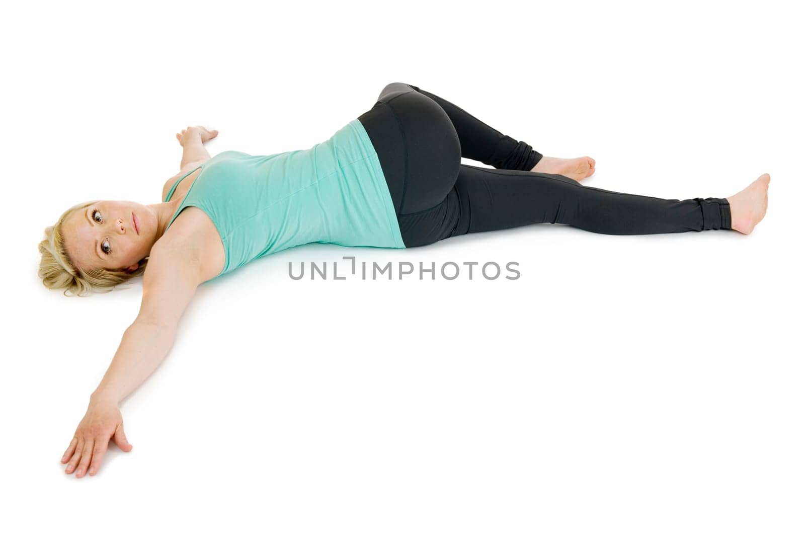Full body view of a young,blonde woman with yoga exercise "supine position twisted"" on white background with light shadows."