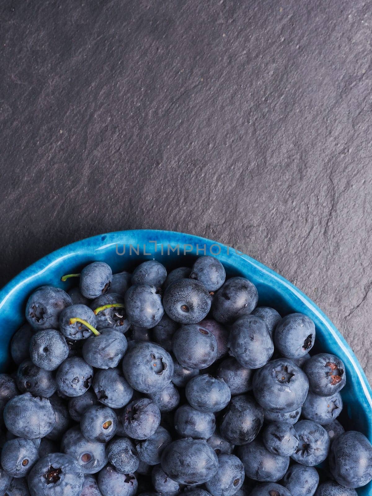 Fresh delicious blueberries in a rustic bowl on dark slate with space for text