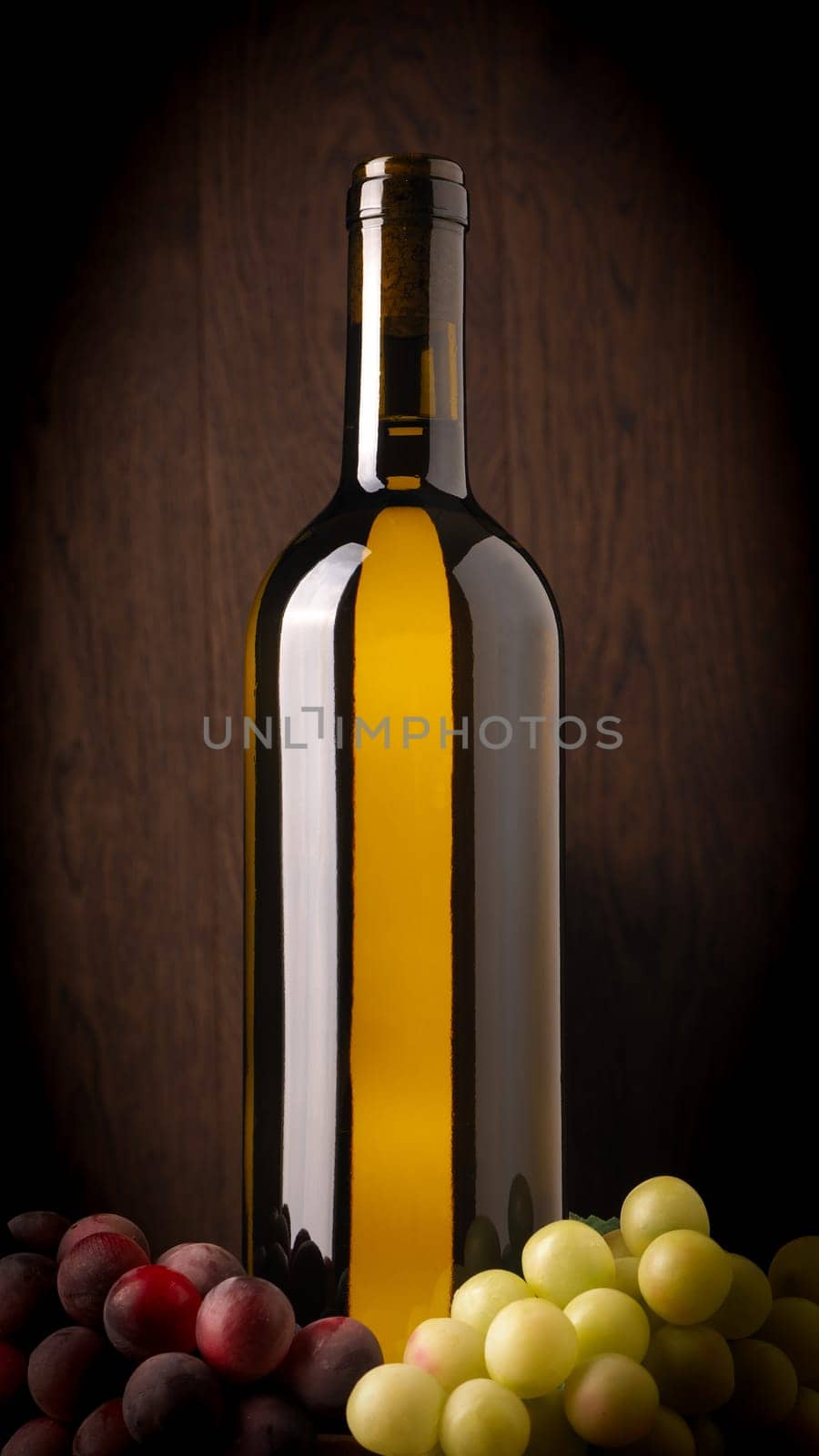 Bottle of white wine with grapes on a dark wooden background