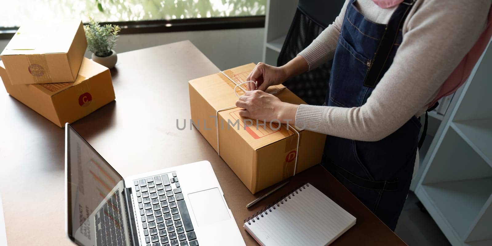 A Muslim entrepreneur seals a package for online sale, highlighting her dedication to business in a contemporary office setting.
