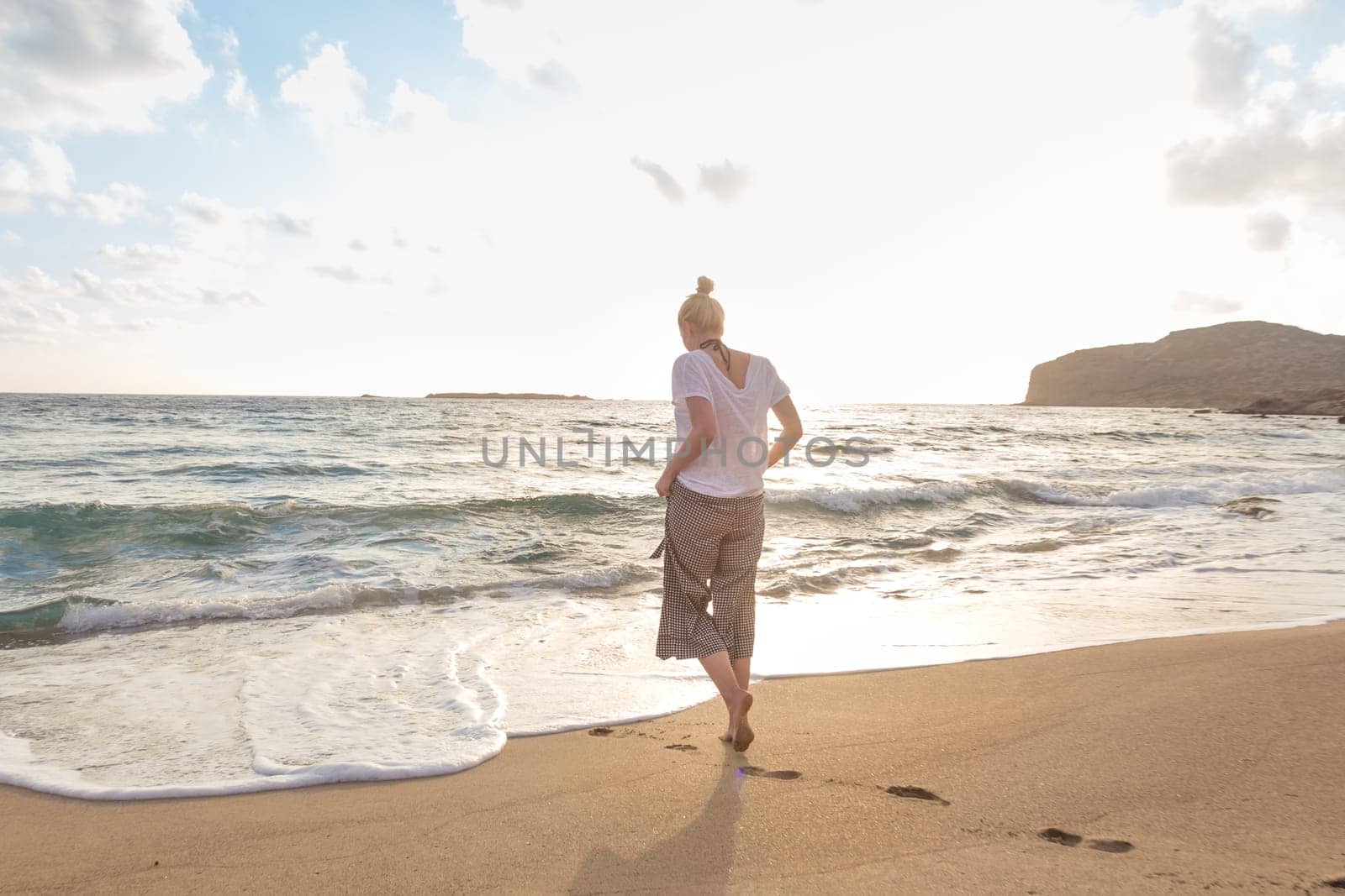 Woman walking on sand beach at golden hour. Seashore sunset walk.