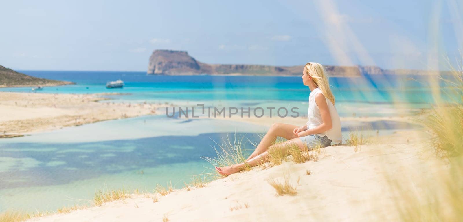 Relaxed woman enjoying sun, freedom and life an a beautiful sandy beach of Balos in Greece. Young lady feeling free, relaxed and happy. Vacations, freedom, happiness, enjoyment and well being.
