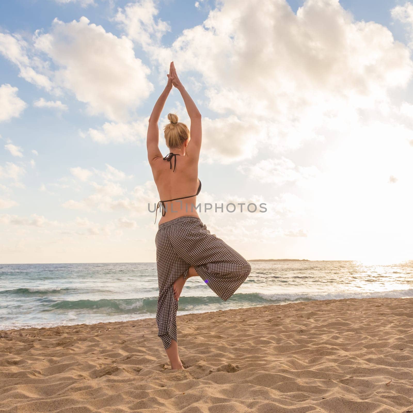 Active young woman practicing yoga on beach at sunset.
