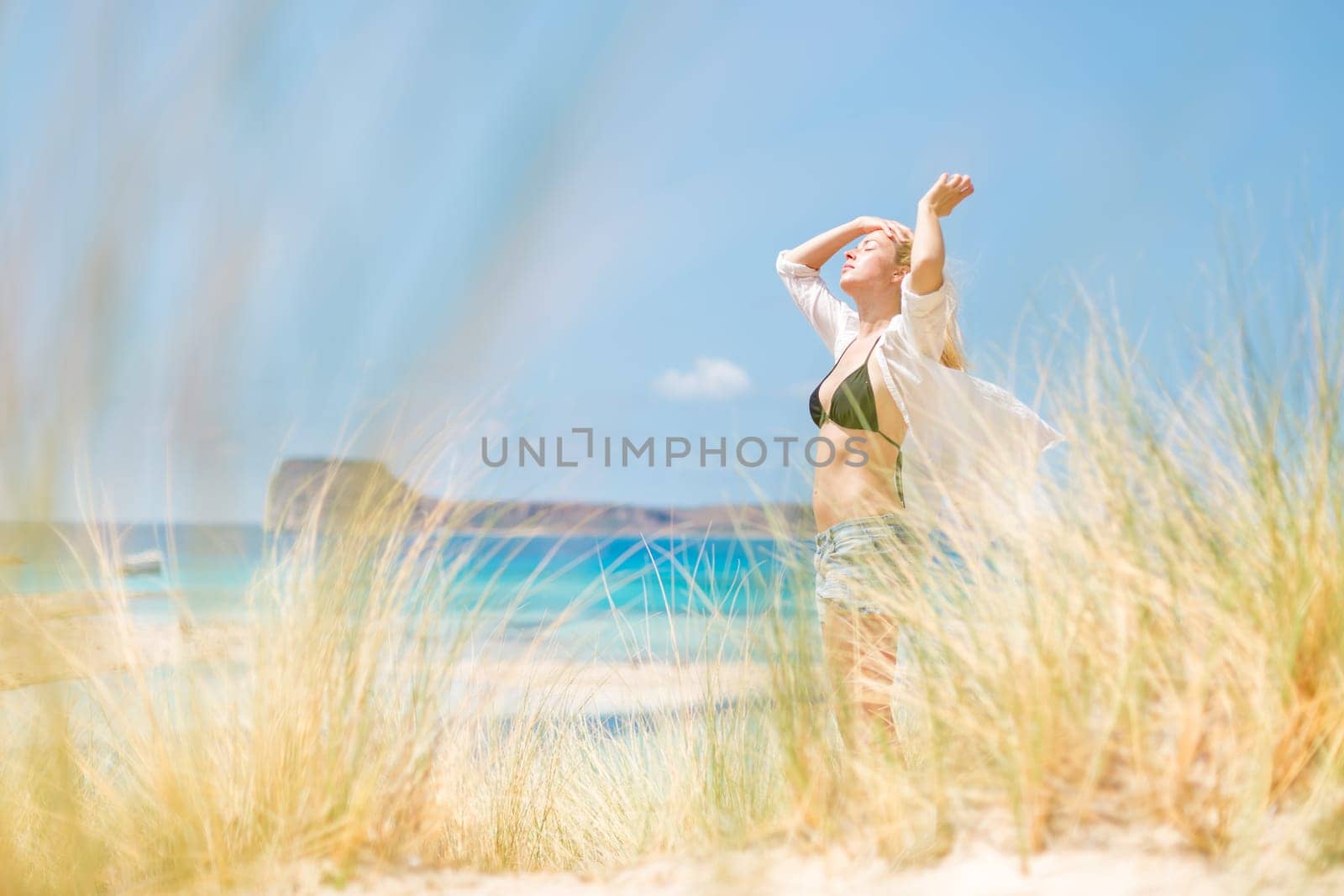 Relaxed woman enjoying sun, freedom and life an a beautiful beach. Young lady feeling free, relaxed and happy. Concept of vacations, freedom, happiness, enjoyment and well being.