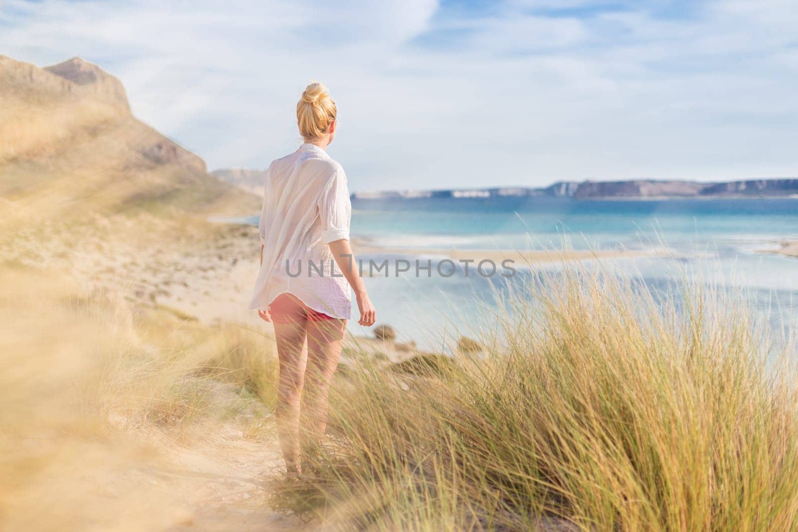 Relaxed woman in white shirt looking at distance, enjoying beautiful nature, freedom and life at serene landscape at Balos beach, Greece. Concept of vacations, freedom, happiness, joy and well being.