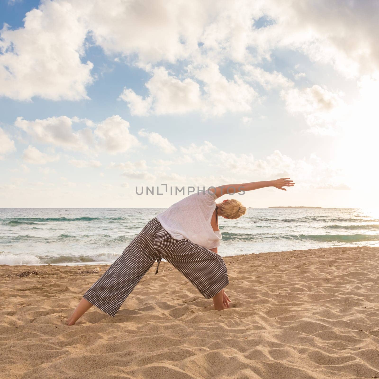 Active young woman practicing yoga on beach at sunset.