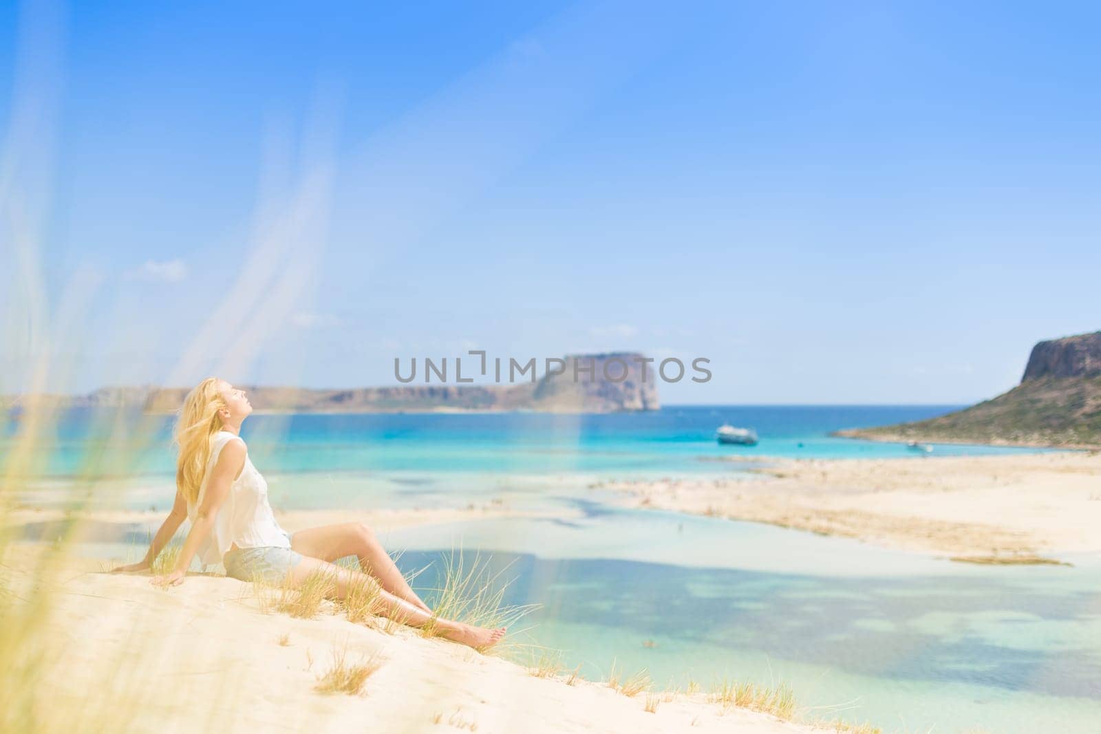 Relaxed woman enjoying sun, freedom and life an a beautiful sandy beach of Balos in Greece. Young lady feeling free, relaxed and happy. Vacations, freedom, happiness, enjoyment and well being.