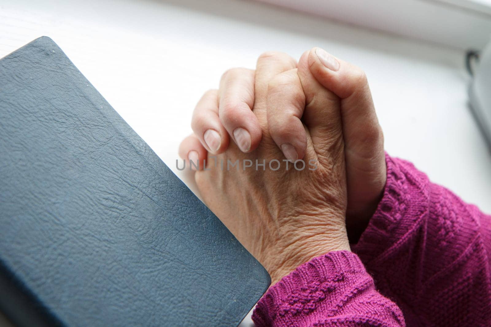 elderly women hands crossed in prayer next to Bible