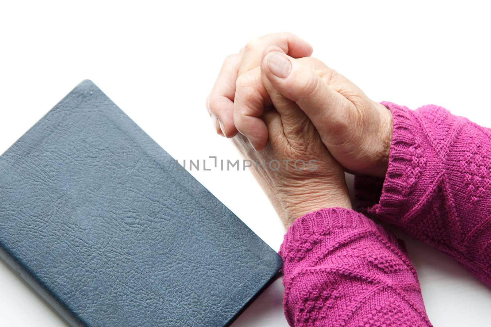 elderly women hands crossed in prayer next to Bible