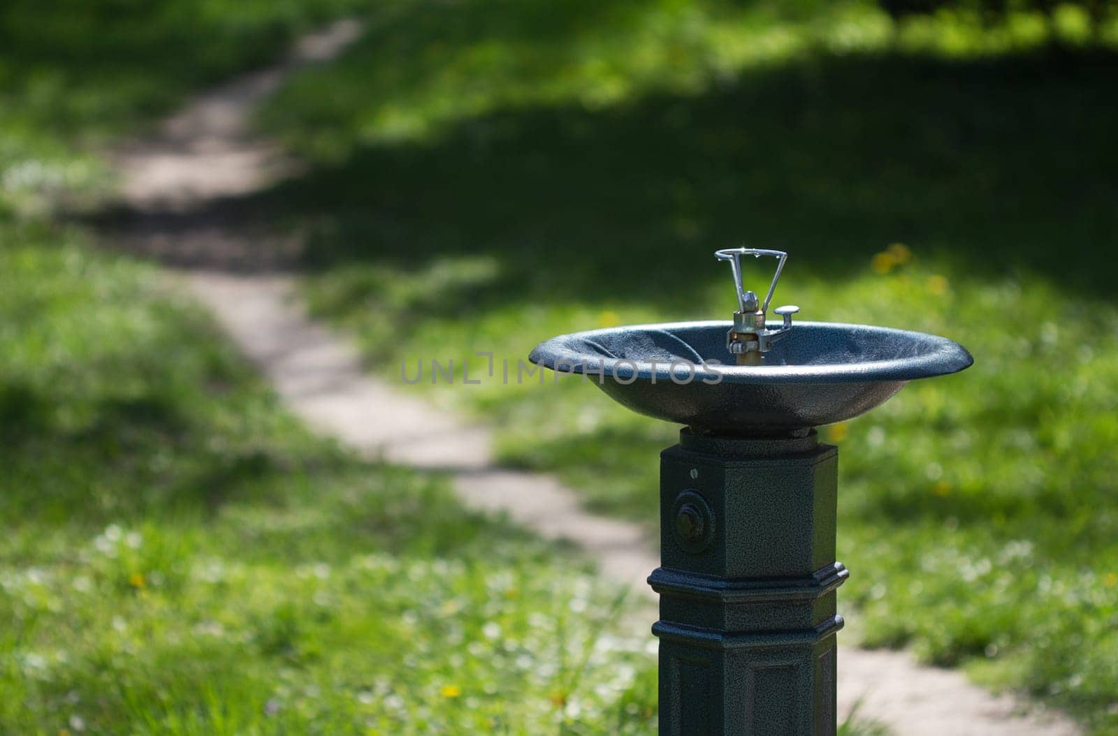 Horizontal close up of a metal water dispenser in a green park