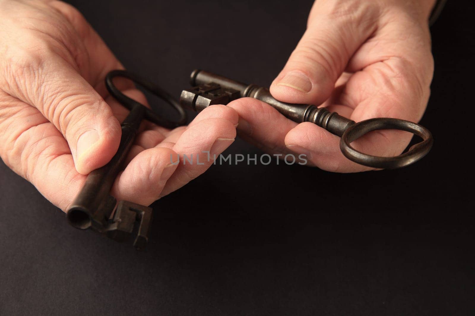 Older man holds two large, old keys on a black surface with copy space.