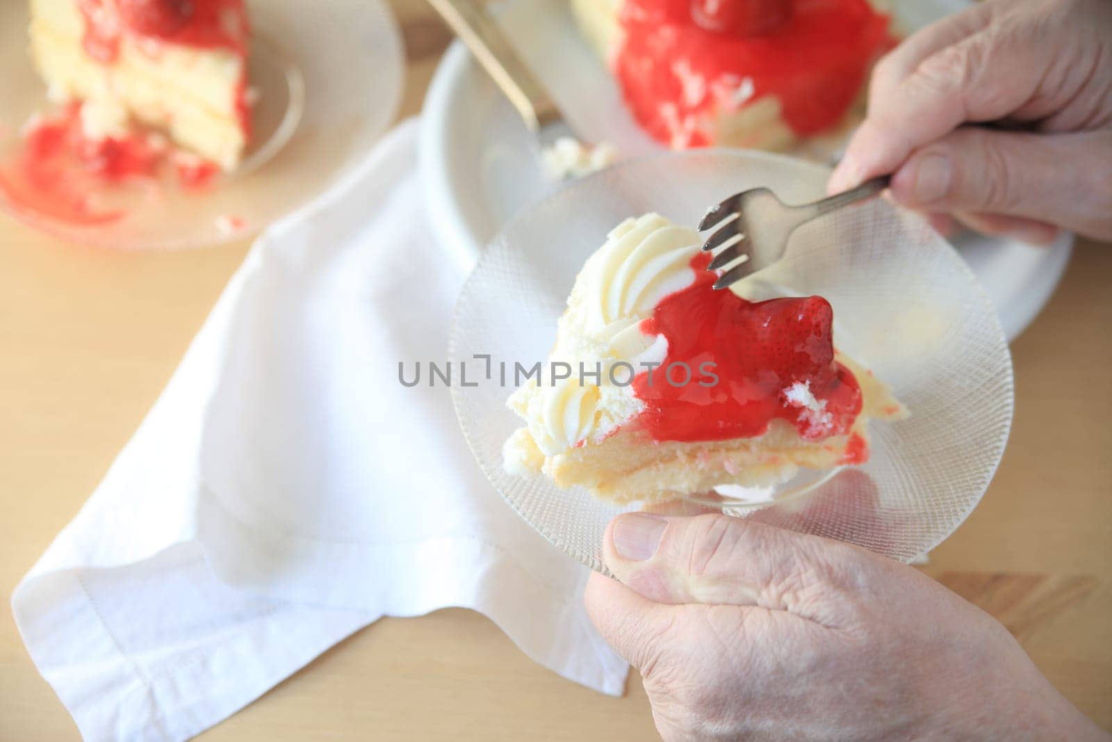 Man holds glass dish with portion of cake with whipped cream and strawberry glaze.